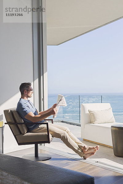 Mann liest entspannt Zeitung im sonnigen Innenhof mit Blick aufs Meer