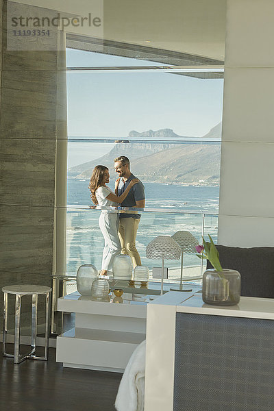 Spiegelung eines sich umarmenden Paares auf einem luxuriösen Balkon mit sonnigem Meer- und Bergblick