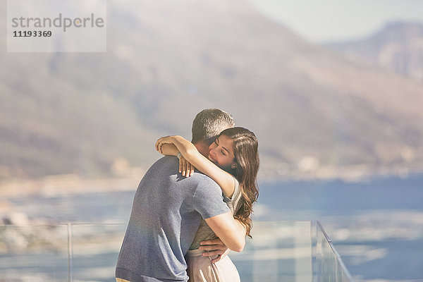 Zärtliches Paar  das sich auf dem Balkon mit Blick auf das Meer und die Berge umarmt