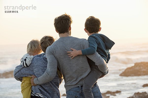 Glückliche junge Familie mit Blick auf das Meer am Strand bei Sonnenuntergang