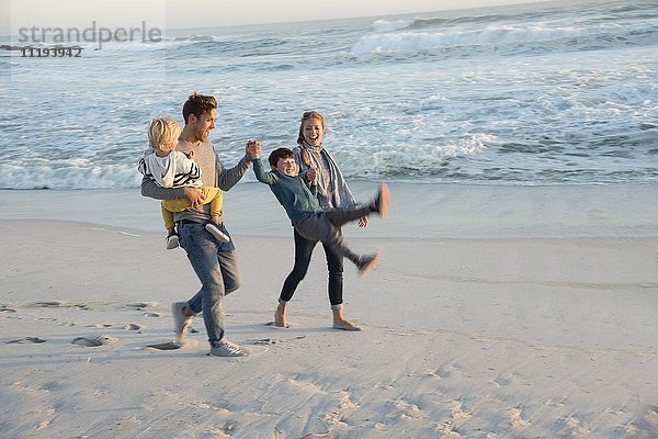 Fröhliche junge Familie mit Spaß am Strand bei Sonnenuntergang