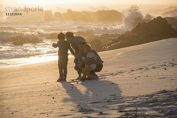 Fröhliche junge Familie am Strand bei Sonnenuntergang