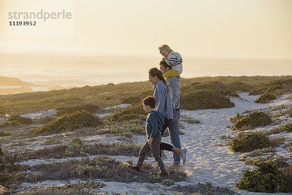 Glückliche junge Familie  die bei Sonnenuntergang am Strand spazieren geht.