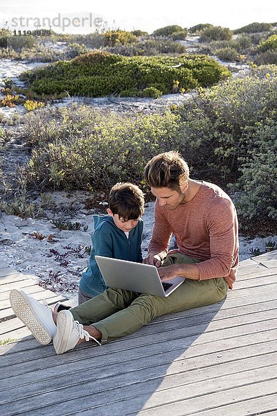 Vater und Sohn mit einem Laptop an der Strandpromenade
