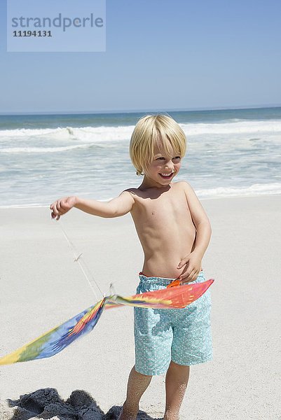 Glücklicher Junge  der einen Drachen am Strand hält.