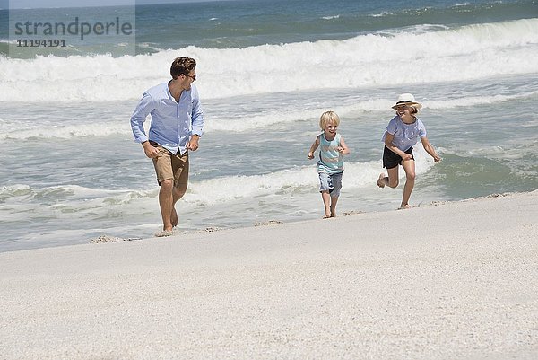 Junger Mann  der mit seinen Kindern am Strand rennt.