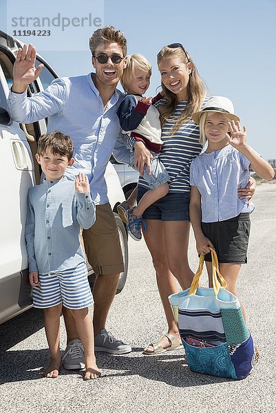 Fröhliche junge Familie steht mit dem Auto für den Urlaub bereit