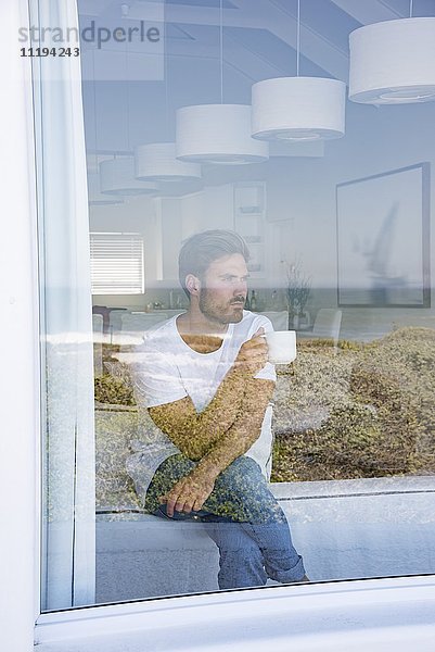 Junger Mann schaut durchs Fenster mit einer Tasse Kaffee.