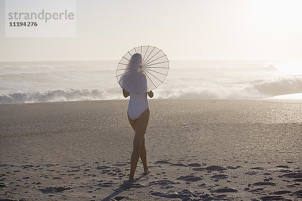 Junge Frau geht mit Sonnenschirm am Strand spazieren