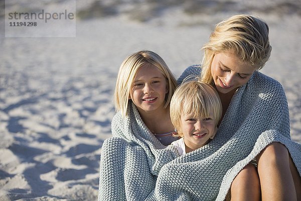 Schöne junge Frau sitzt mit ihren Kindern am Strand.