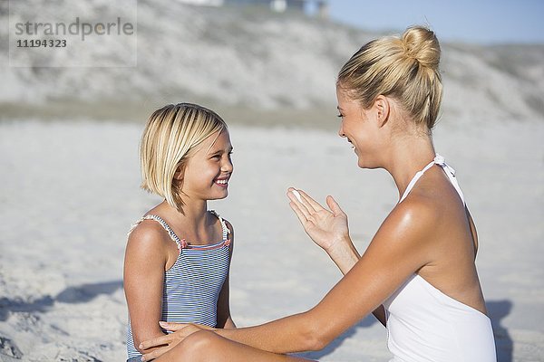Mutter und Tochter lächeln sich am Strand an.