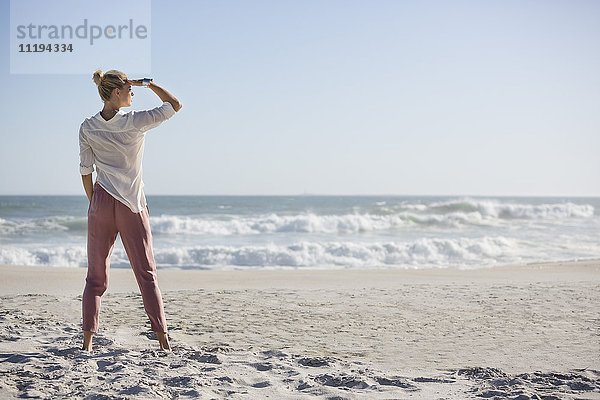 Schöne junge Frau am sonnigen Strand stehend