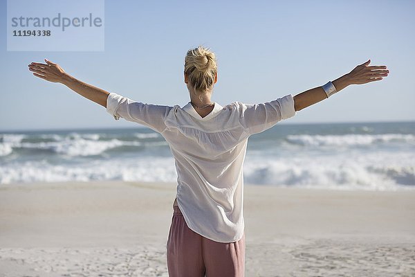 Schöne junge Frau mit ausgestrecktem Arm am sonnigen Strand