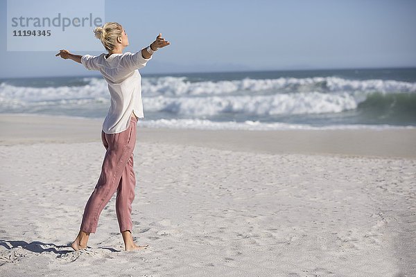 Schöne junge Frau mit ausgestrecktem Arm am sonnigen Strand
