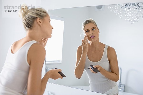 Schöne junge Frau  die Feuchtigkeitscreme auf ihr Gesicht im Badezimmer aufträgt.