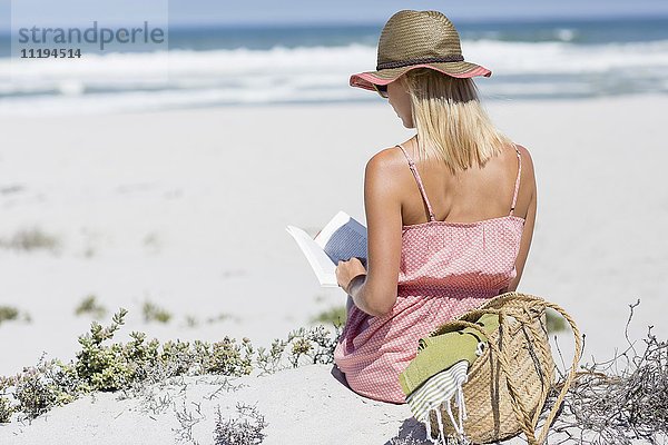 Schöne Frau  die ein Buch am Strand liest.