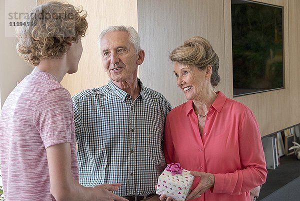Glückliche Großeltern und Teenager-Enkel mit Geburtstagsgeschenk zu Hause