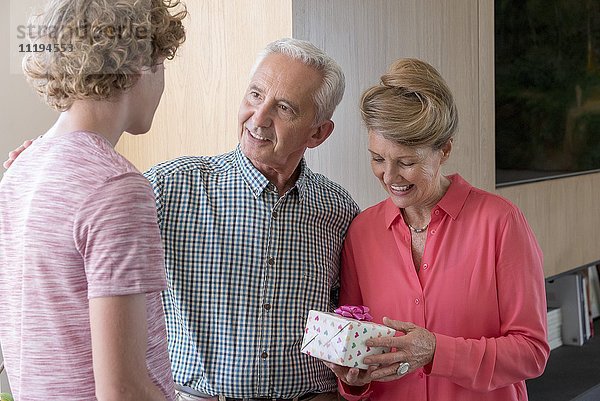 Glückliche Großeltern und Teenager-Enkel mit Geburtstagsgeschenk zu Hause