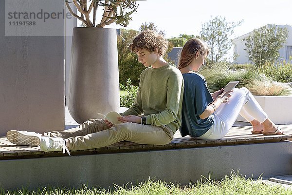 Bruder und Schwester sitzen Rücken an Rücken mit Buch und Tafel im Garten