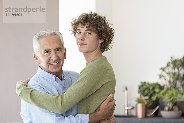 Porträt eines glücklichen älteren Mannes  der seinen jugendlichen Enkel umarmt.