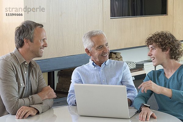 Glücklicher älterer Mann  der einen Laptop mit Sohn und Enkel in einem Wohnzimmer benutzt.