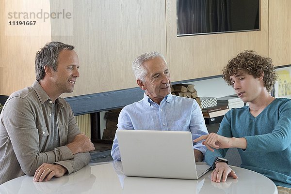 Senior Mann mit einem Laptop mit Sohn und Enkel in einem Wohnzimmer