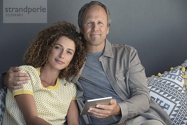 Porträt eines Paares  das auf einer Couch mit einem digitalen Tablett sitzt.