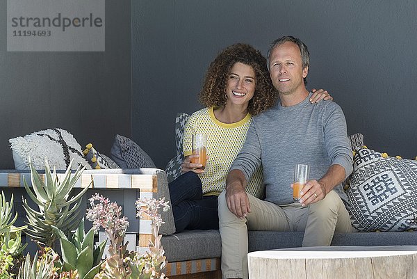 Glückliches Paar sitzt auf einer Couch und trinkt Gemüsesaft.