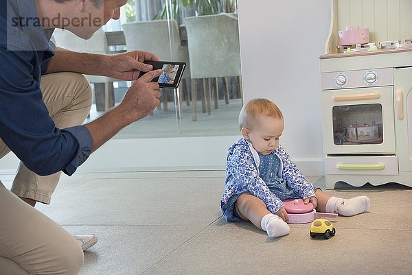 Reifer Mann beim Fotografieren ihrer kleinen Tochter  die mit Spielzeug spielt.