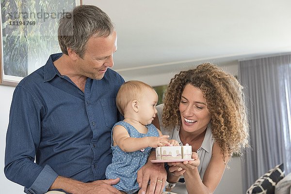 Glückliche Frau  die ihrer kleinen Tochter  die auf dem Schoß ihres Vaters sitzt  Spielzeug schenkt.