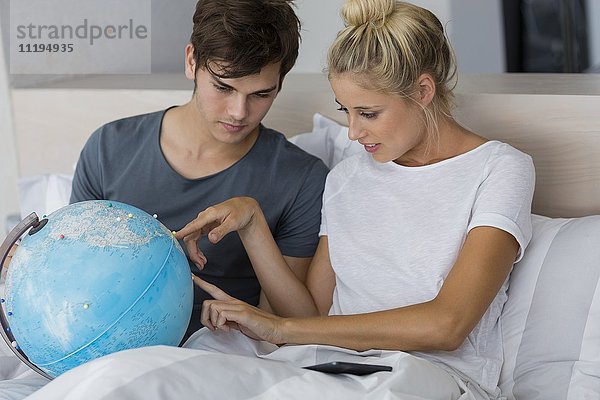 Ein Paar  das auf dem Bett sitzt  bespricht eine Reise in den Urlaub mit Blick auf den Globus.