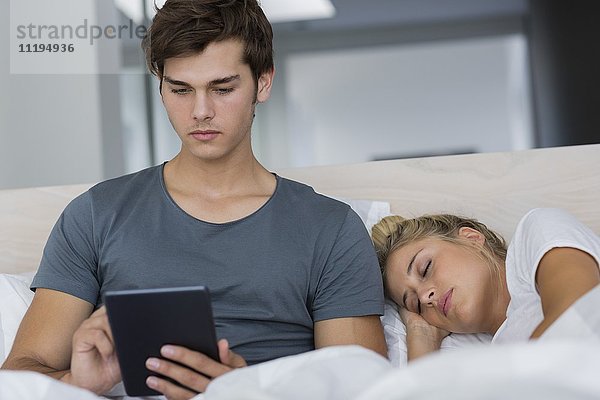 Mann  der ein digitales Tablett benutzt  während seine Freundin in seiner Nähe schläft.