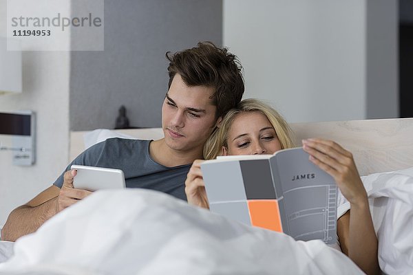 Junge Frau beim Lesen eines Buches mit ihrem Freund auf einem digitalen Tablett