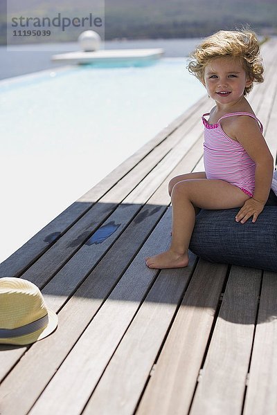 Fröhliches kleines Mädchen sitzt auf einer Promenade