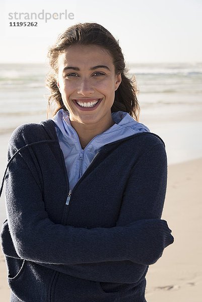 Hübsche junge Frau am Strand stehend und lächelnd