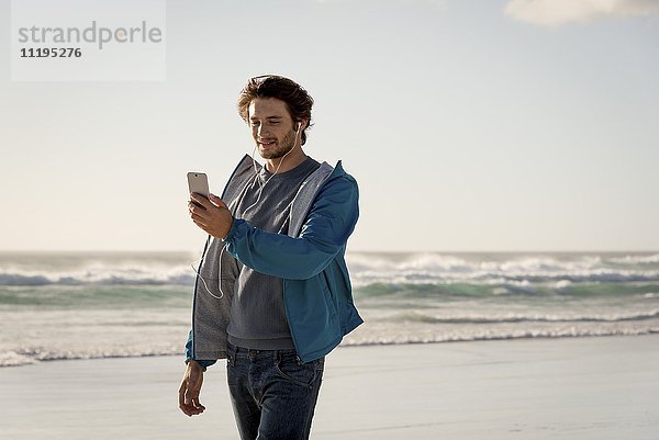 Glücklicher junger Mann mit einem Telefon am Strand