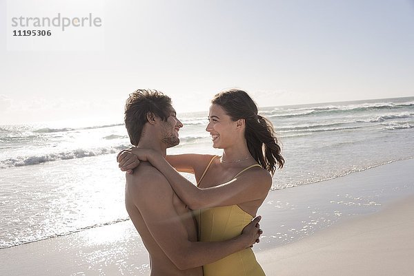 Ein glückliches junges Paar  das sich am Strand umarmt.