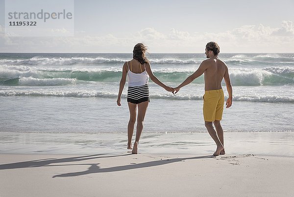 Rückansicht eines jungen Paares beim Spaziergang am Strand