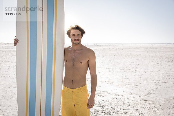 Glücklicher junger Mann mit Surfbrett am Strand