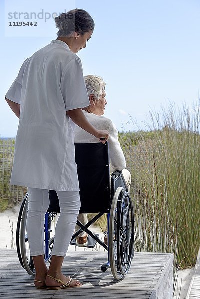 Krankenschwester assistiert Senior im Rollstuhl im Freien
