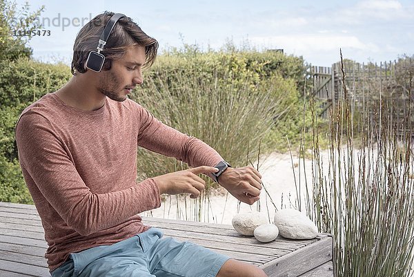 Junger Mann mit seiner intelligenten Uhr und Musik hören über Kopfhörer