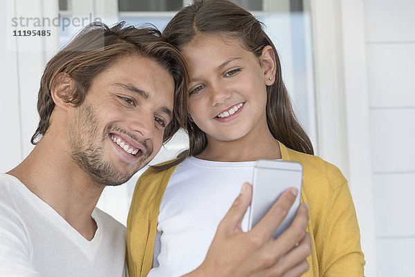 Glücklicher Vater mit seiner kleinen Tochter  die einen Selfie mit Fotohandy mit nach Hause nimmt.