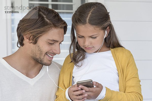 Glücklicher Vater mit seiner kleinen Tochter beim Musikhören auf dem Handy mit Ohrhörern