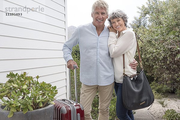 Glückliches Seniorenpaar steht mit Koffer vor dem Haus
