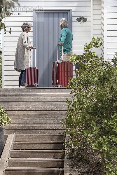 Seniorenpaar mit Koffer wartet vor der Haustür