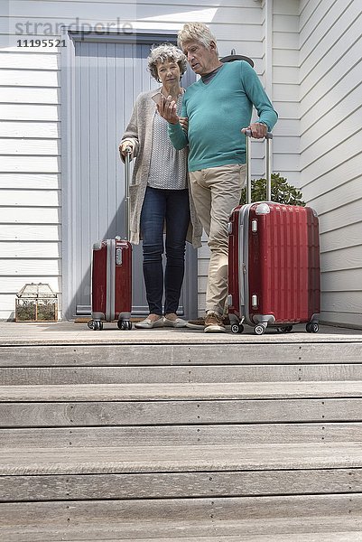Seniorenpaar mit Koffer über Smartphone an der Haustür