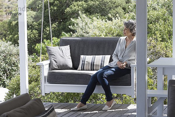 Fröhliche Frau entspannt sich auf dem Schaukelstuhl auf der Veranda