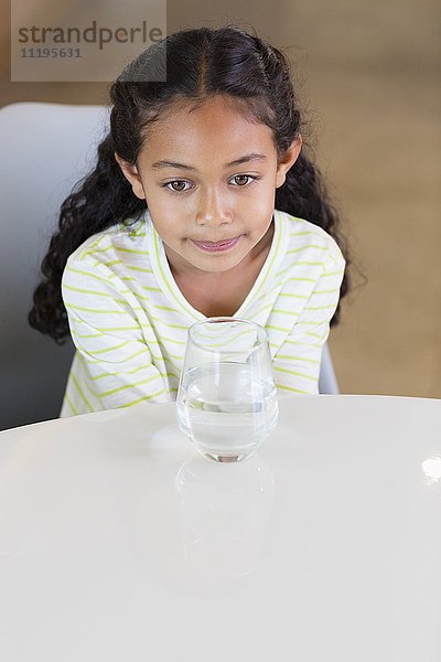Kleines Mädchen mit einem Glas Wasser auf dem Tisch