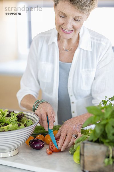 Glückliche Seniorin beim Schneiden von Gemüse in der Küche