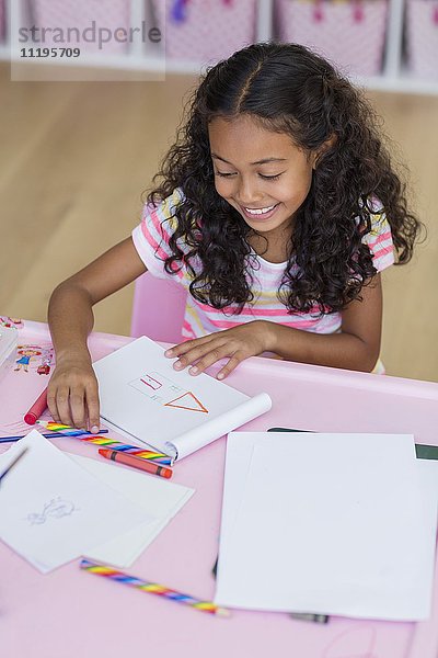 Glückliches kleines Mädchen bei den Hausaufgaben auf dem Tisch